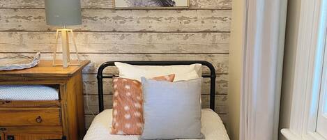 A neatly made bed with pillows and a folded towel on a wooden table beside it.