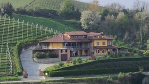 A two-story house with a balcony, surrounded by terraced vineyards and lush greenery. - CASA CASTELLA (Diano d'Alba)