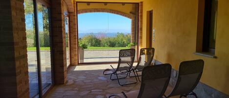 A covered outdoor seating area with stone flooring and a view of greenery and mountains in the distance.