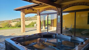 A hot tub area with a stone floor, a pergola with brick pillars, and a glass door leading to a yellow building. - CASA CASTELLA (Diano d'Alba)