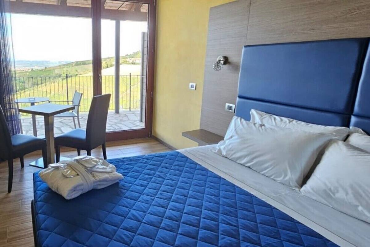 Habitación de hotel con una cama grande, una pequeña mesa con sillas y vistas al campo a través de una puerta corredera.
