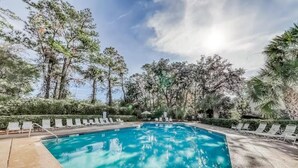 Une piscine entourée de chaises longues et d’arbres.