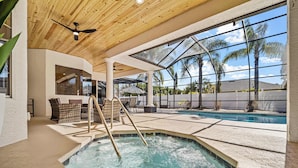 Un área de piscina interior con techo de madera, ventanas amplias y vistas a palmeras.