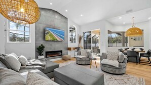 Una sala de estar moderna con chimenea, sofás grises, un televisor grande y un comedor con mesa y sillas.