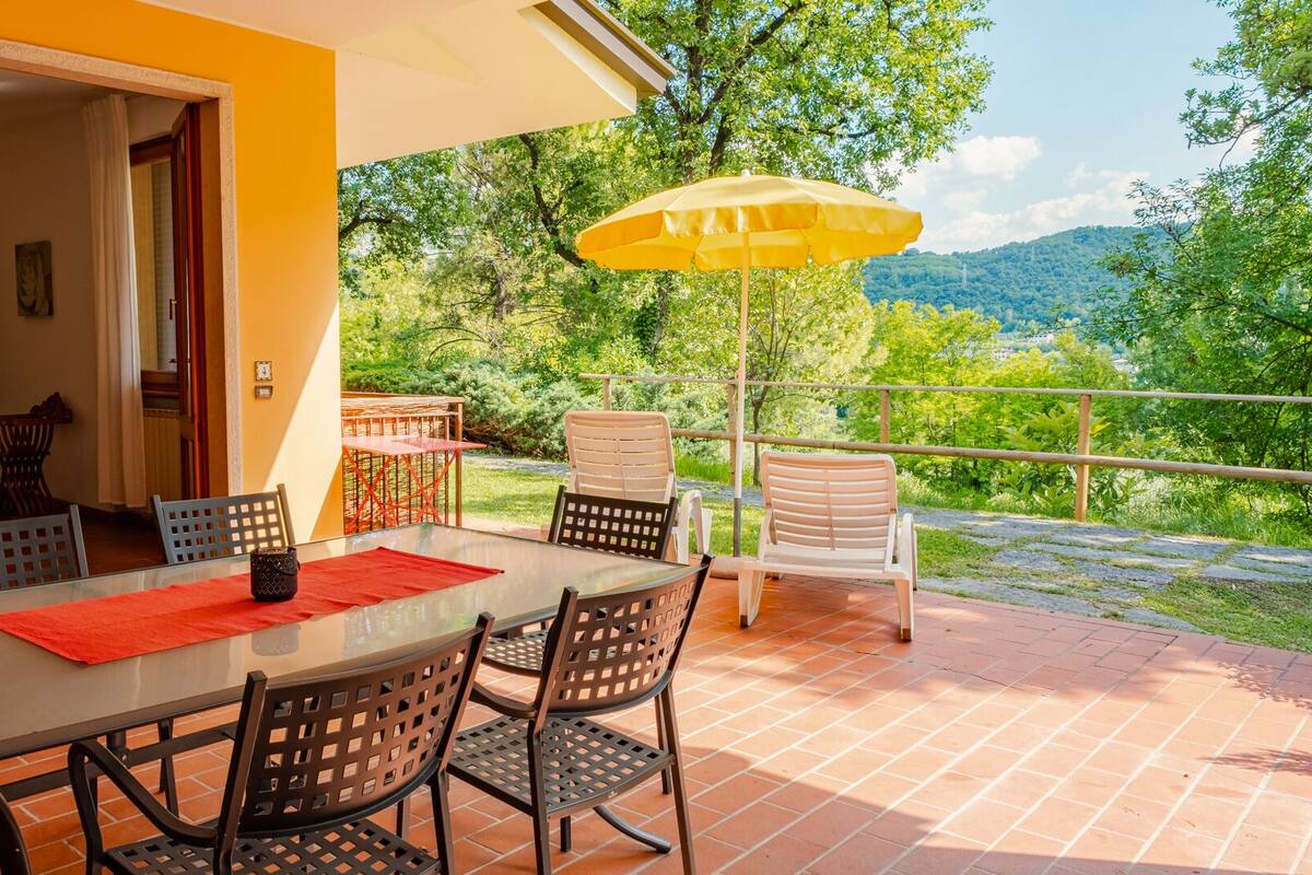Une terrasse avec une table et des chaises, un parasol jaune et une vue sur un paysage verdoyant.