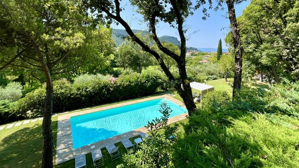 A swimming pool surrounded by lush greenery and trees, with a clear view of the landscape in the background. - Residence Casa Adriana (Costermano sul Garda)