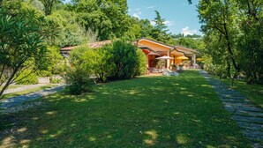 A villa with a paved driveway leading to a covered patio area with outdoor furniture. - Residence Casa Adriana (Costermano sul Garda)