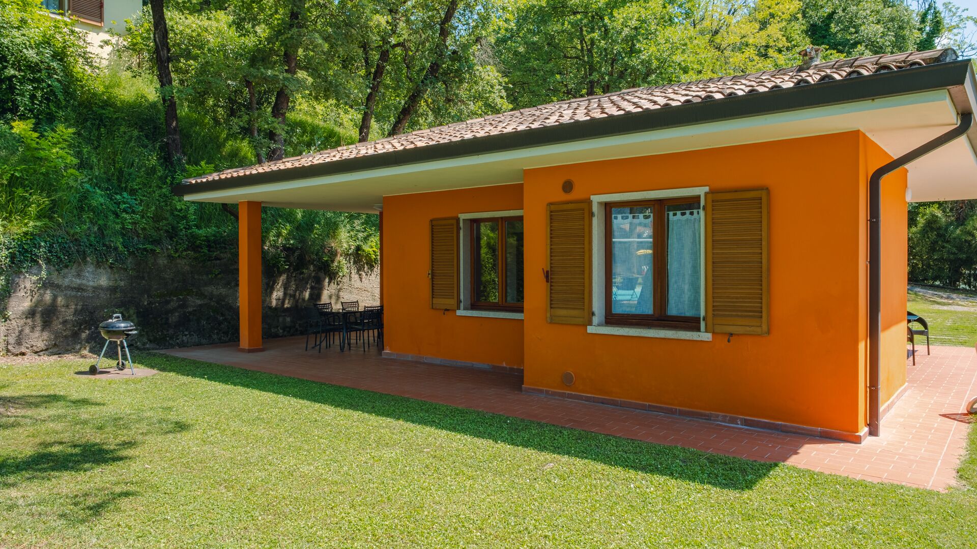 A two-story building with a tiled roof, orange walls, and a covered patio area with outdoor furniture.