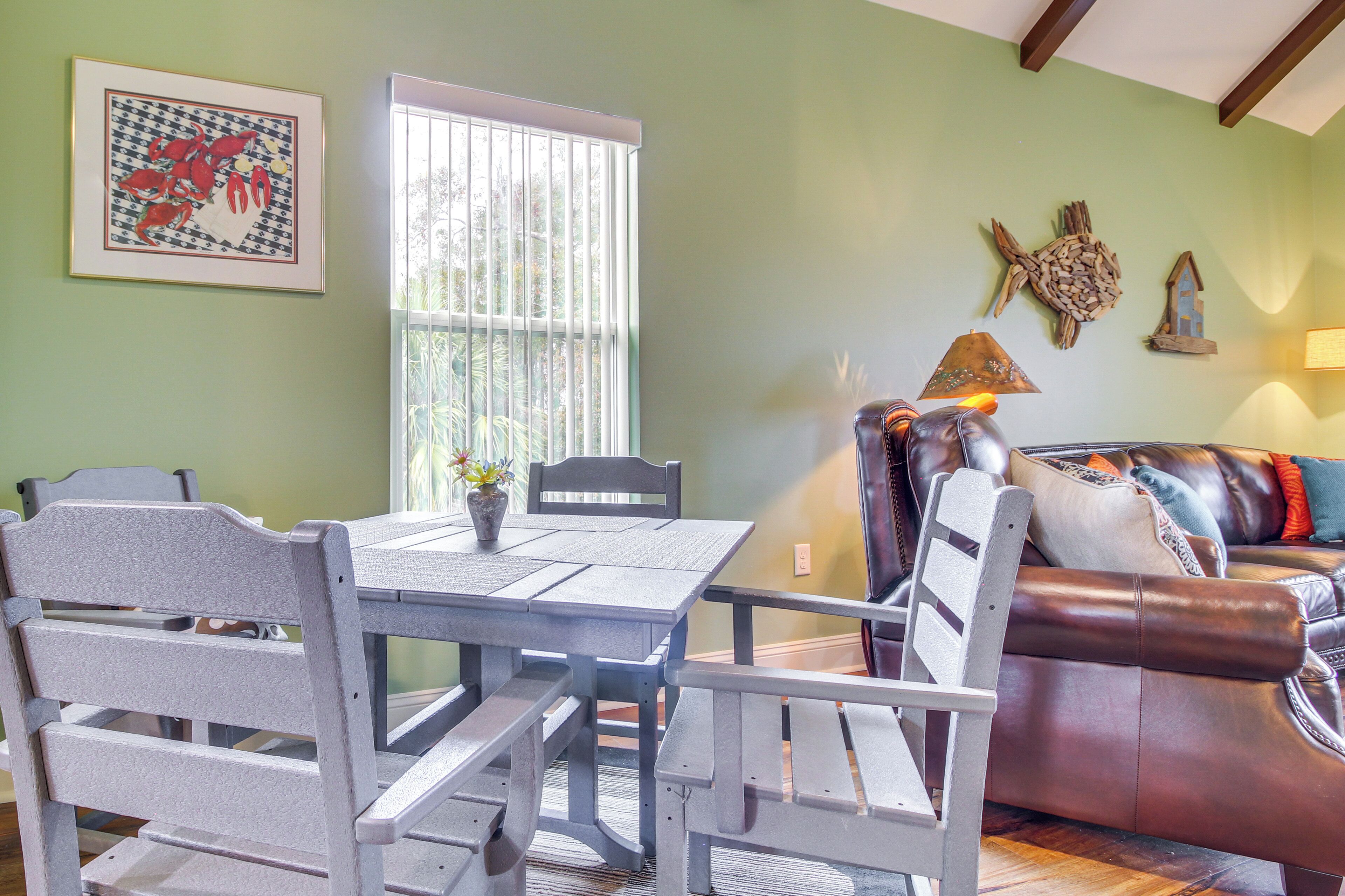 Un coin repas avec une table et des chaises, une fenêtre avec des stores, un canapé et des éléments décoratifs sur les murs.