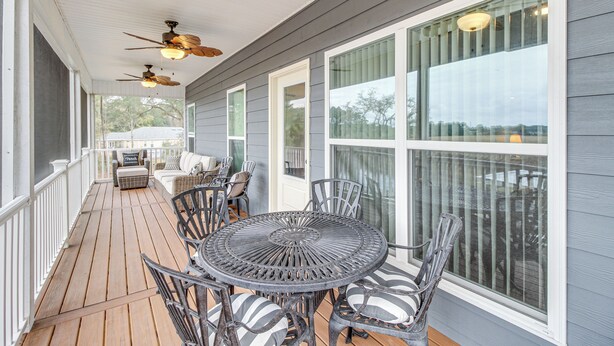 A covered porch with a round metal table and chairs, a sofa, and ceiling fans. - Dock & Fire Pit: Waterfront Midway Retreat! (Midway)