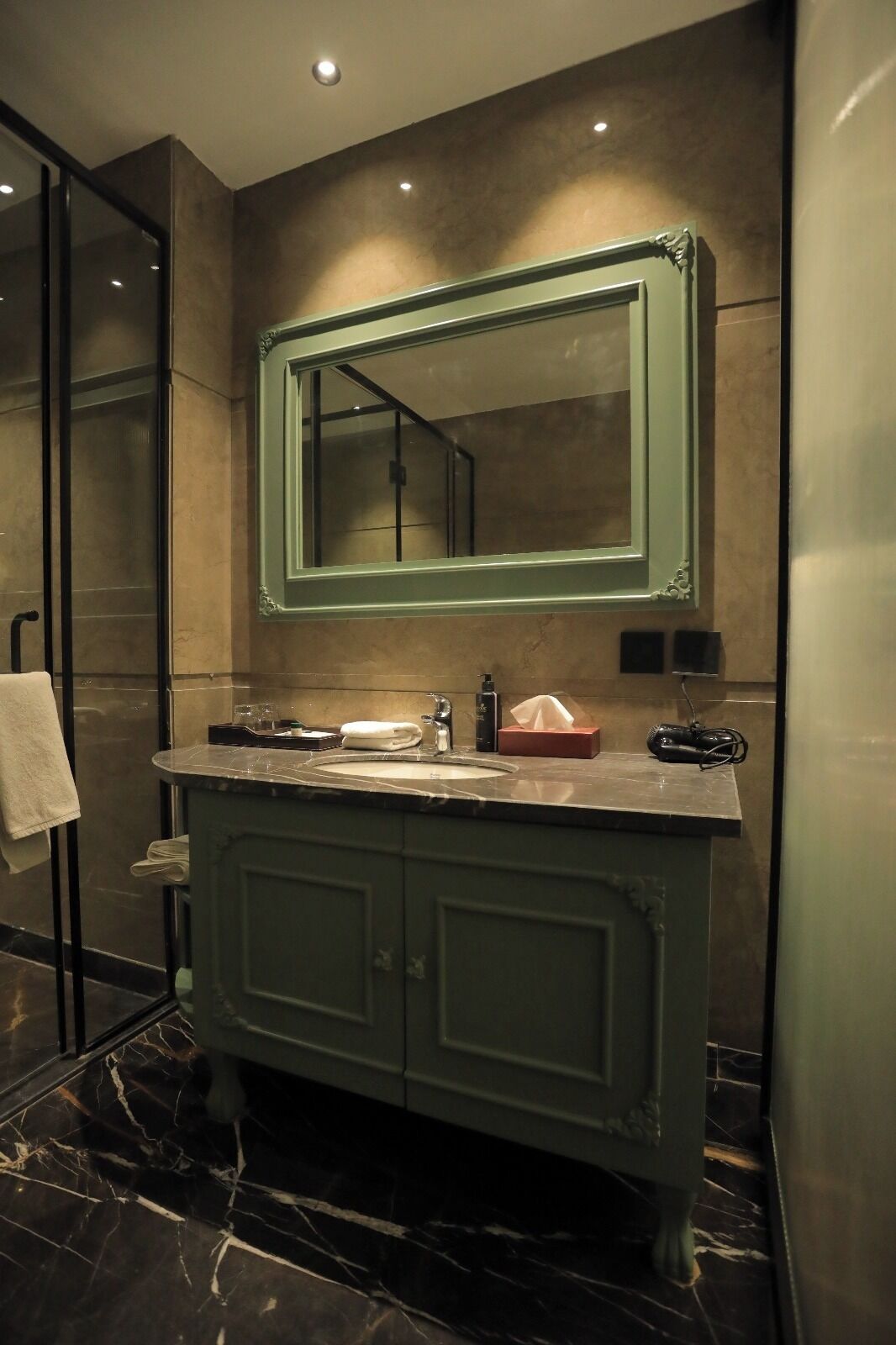 A bathroom with a marble sink, a green vanity, a large mirror, and a towel rack.
