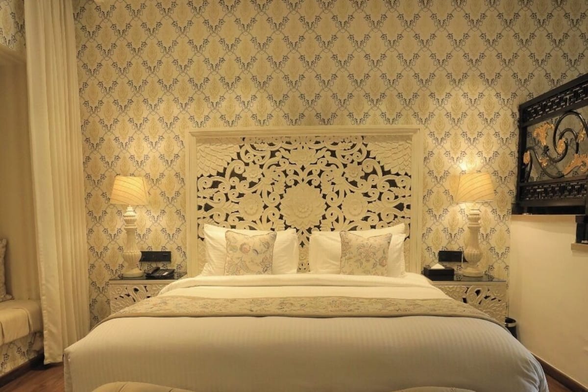 A large bed with a tufted headboard, two bedside tables with lamps, and a patterned wallpaper.