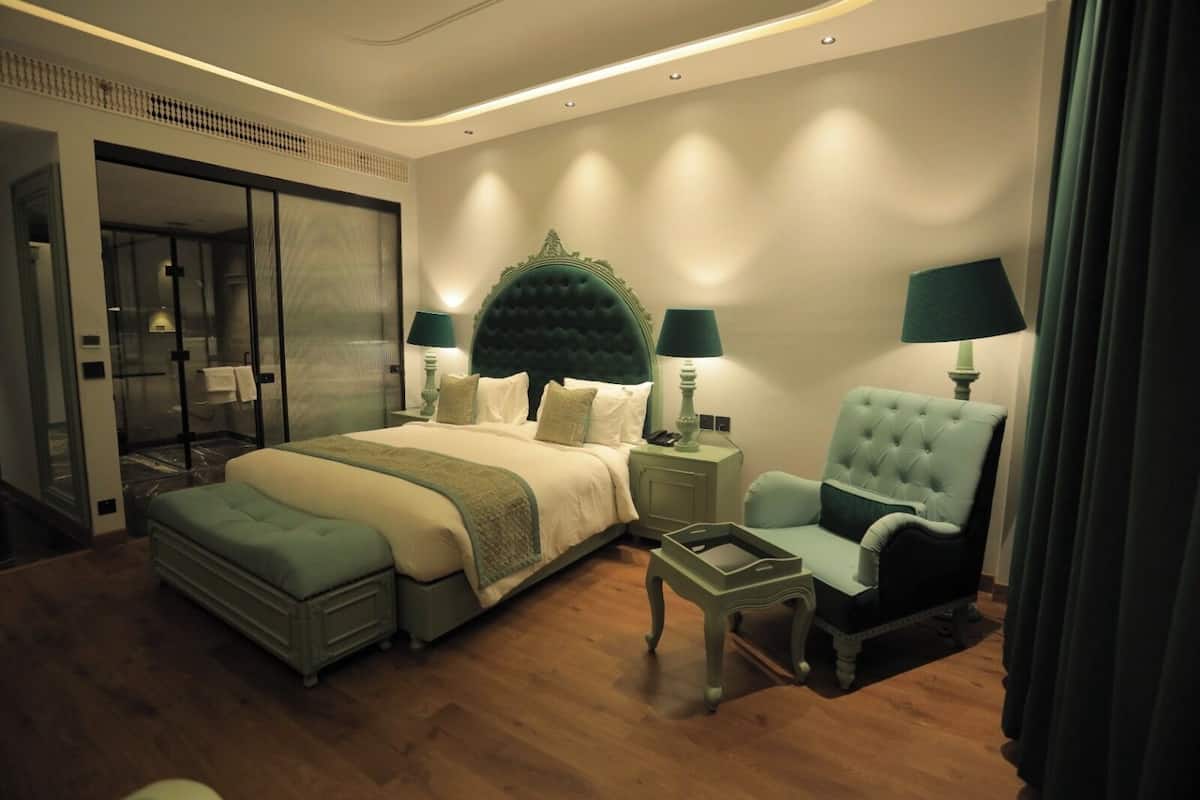 A hotel room with a large bed, a seating area with a chair and a small table, and a glass-enclosed shower area.