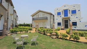 A courtyard with a lawn, a white building with blue accents, and a traditional entrance. - THE ROYAL VENETIAN (Samalkha)