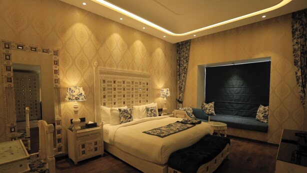 A spacious bedroom with a large bed, bedside tables, a nightstand, a sofa, and a window with curtains. - THE ROYAL VENETIAN (Samalkha)