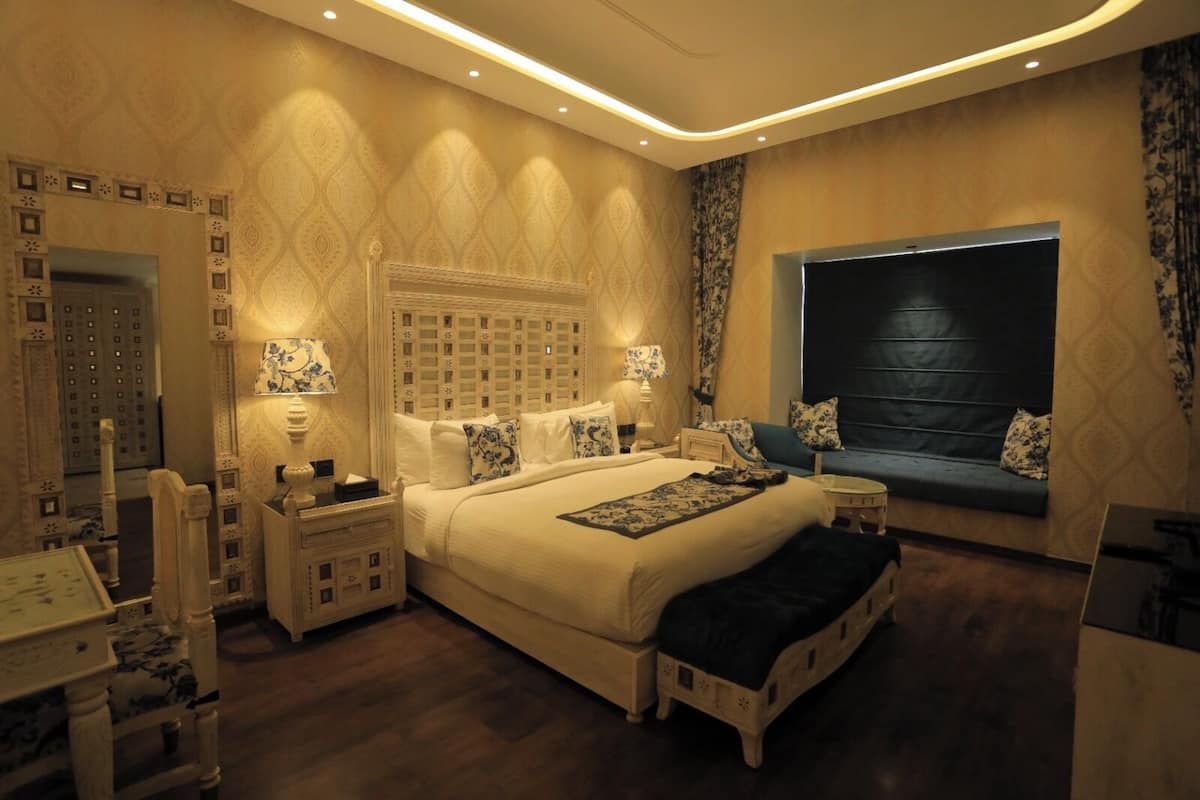 A spacious bedroom with a large bed, bedside tables, a nightstand, a sofa, and a window with curtains.