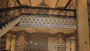 A dining area with a checkered floor, a round table, and chairs. There is a staircase with a decorative railing, and patterned wallpaper on the walls. - THE ROYAL VENETIAN (Samalkha)
