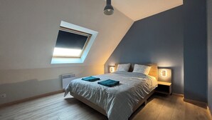 A bedroom with a sloped ceiling, a skylight, a bed with a headboard, bedside lamps, and a radiator. - Home. Pointe des Espagnols. (Roscanvel)