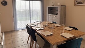 A dining area with a wooden table set for four, chairs, a cabinet with shelves, a clock, and a window with curtains. - Home. Pointe des Espagnols. (Roscanvel)