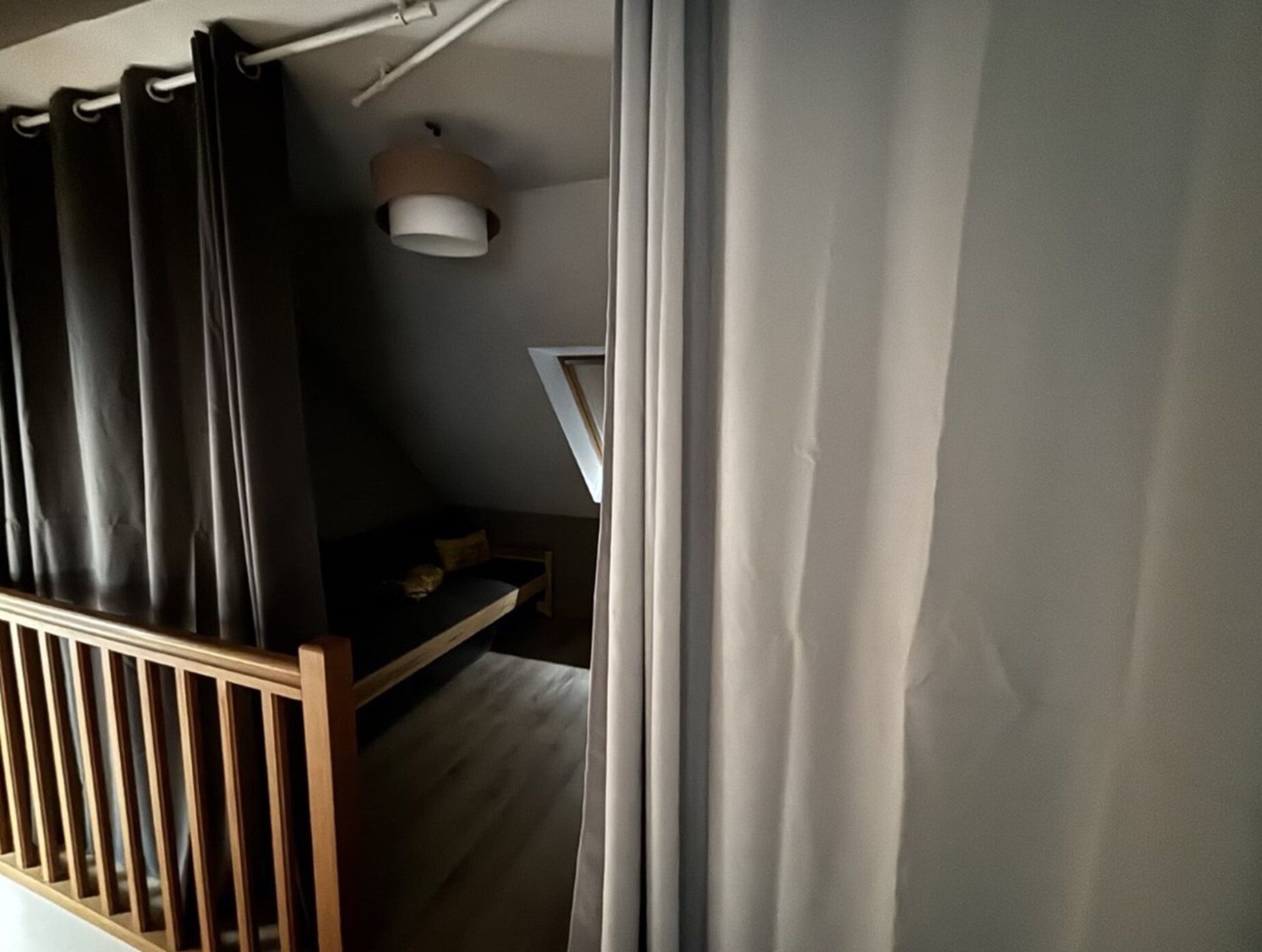 A bedroom with a sloped ceiling, a bed, a small desk, and a hanging light fixture.