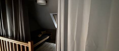A bedroom with a sloped ceiling, a bed, a small desk, and a hanging light fixture.