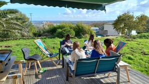 A group of people sitting on deck chairs under a canopy, with a grassy area and a view of the sea in the background. - Home. Pointe des Espagnols. (Roscanvel)