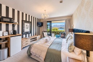 Une chambre avec un grand lit, un bureau avec un ordinateur, une télévision et une vue sur un lac.