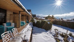 Ein überdachter Außenbereich mit weißen Stühlen und einer Holzterrasse, mit Blick auf eine verschneite Landschaft und Berge im Hintergrund.
