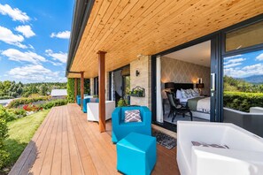 Une terrasse extérieure moderne, dotée d’un plancher en bois et de mobilier bleu et blanc, qui donne accès à une pièce avec un lit et une vue sur l’extérieur.
