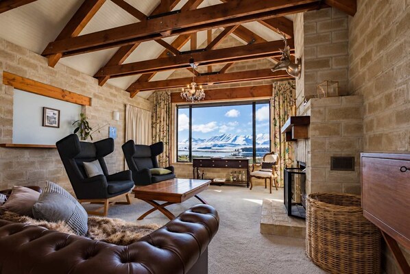 A spacious living room with a large window offering a mountain view, wooden beams on the ceiling, and a cozy seating area with a leather sofa and chairs. - Tekapo Private Room | Lake + Mountain Views (Lake Tekapo)