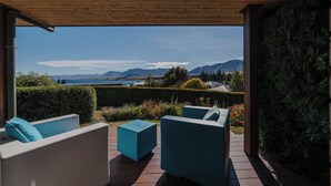 Een overdekt terras met moderne meubels, uitzicht op bergen en een waterpartij.