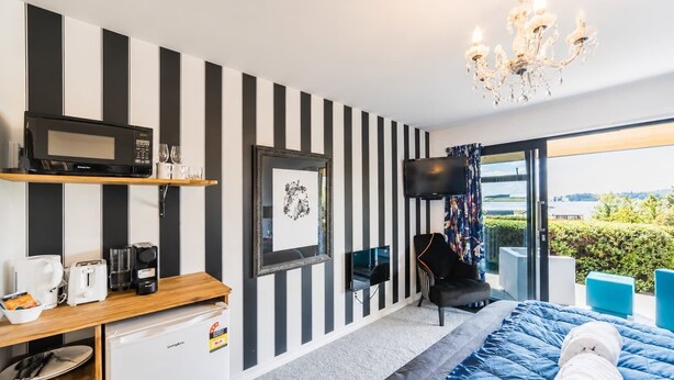 Een moderne hotelkamer met een zwart-wit gestreepte wand, een flatscreen televisie, een bed met een blauwe sprei, een klein bureau met een magnetron, en uitzicht op de omgeving.