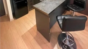 Eine moderne Küche mit einem schwarzen Kühlschrank, einer Mikrowelle und einer Bar mit zwei schwarzen Barhocker.