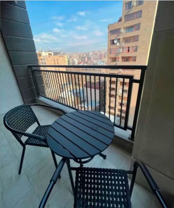 A balcony with a round table and two chairs, overlooking a cityscape with buildings.