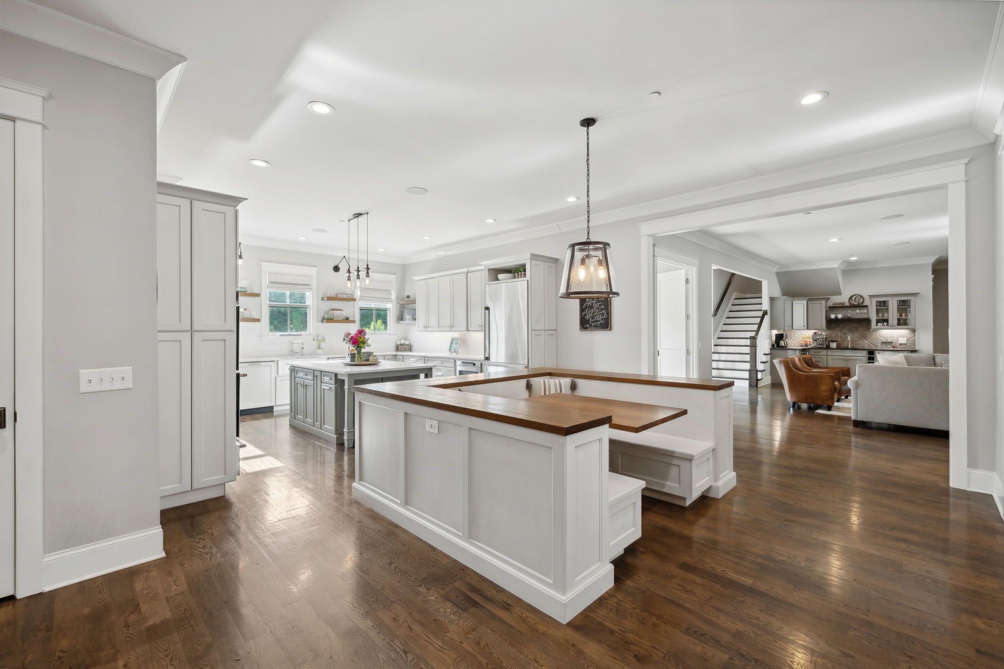 A spacious kitchen with white cabinetry, a central island, and a staircase leading to an upper level.