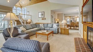 A spacious living room with a high ceiling, a large sofa, a coffee table, and a dining area with chairs and a table. - Cheven, Ships Watch Community in Duck, NC (Kitty Hawk)