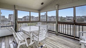 A covered outdoor area with a wooden table and chairs, large windows offering views of buildings and a beach. - Cheven, Ships Watch Community in Duck, NC (Kitty Hawk)