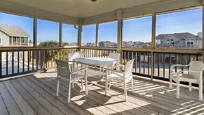 A covered outdoor deck with a table and chairs, large windows, and a ceiling fan. - Little, Ships Watch Community in Duck, NC (Kitty Hawk)