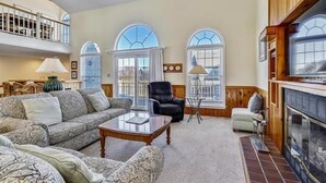 A spacious living room with a fireplace, a sofa set, and a high ceiling with wooden beams. - Little, Ships Watch Community in Duck, NC (Kitty Hawk)