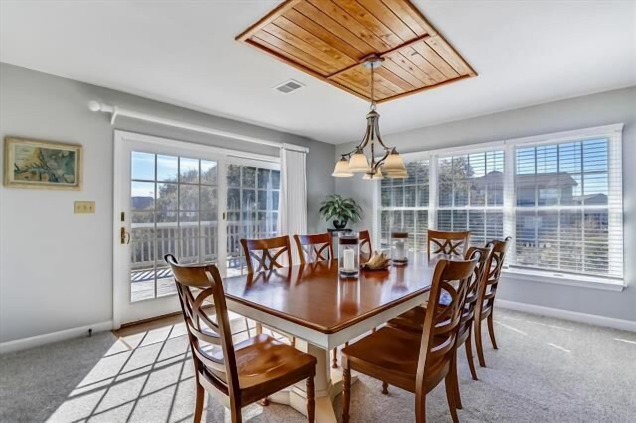 A dining area with a wooden table and chairs, large windows, and a ceiling fan.