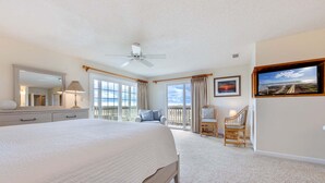 A spacious bedroom with a large bed, a ceiling fan, a balcony with a view, and a television. - Spendlove, Ships Watch Community in Duck, NC (Duck)
