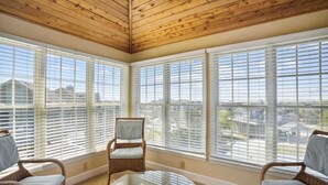 Un solárium con ventanas amplias, mobiliario de mimbre y una mesa de vidrio.