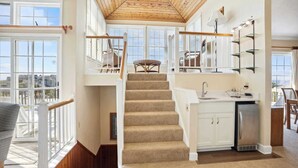 Un interior espacioso con una escalera de madera, una zona de cocina y amplios ventanales que ofrecen vistas al exterior.