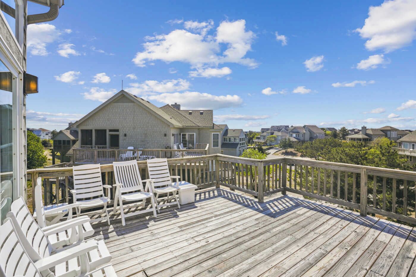 A wooden deck with white chairs and a view of a house with a balcony.