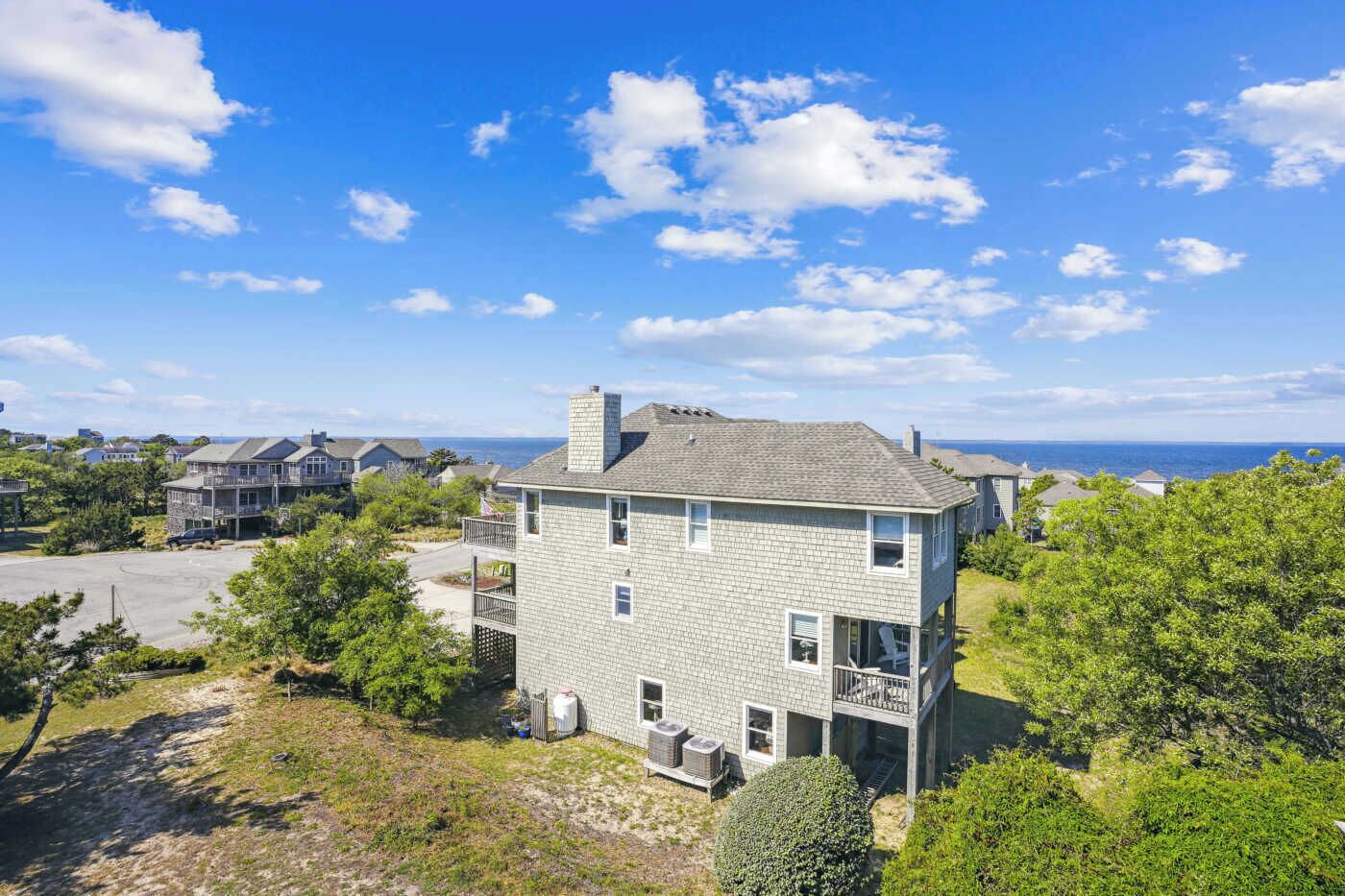A two-story house with a balcony, surrounded by greenery and a clear view of the ocean.