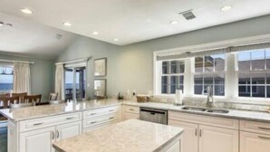 A spacious kitchen with white cabinetry, a granite countertop, and a large window providing a view of the outdoors. - Hemmington, Ships Watch Community in Duck, NC (Duck)