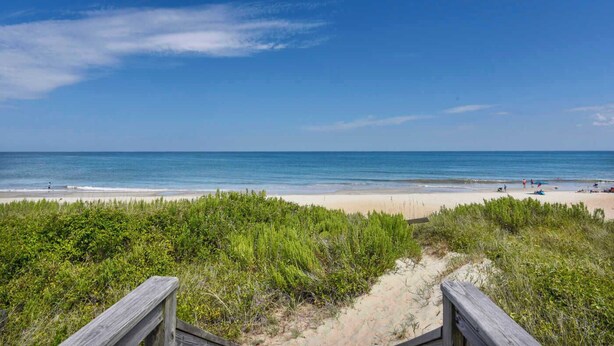 A beach with a wooden boardwalk leading to the shore, clear blue sky, and calm sea. - Hemmington, Ships Watch Community in Duck, NC (Duck)