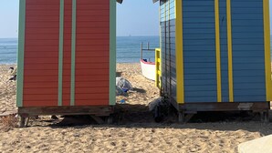 Dos cabañas de playa, una roja y otra azul, con un bote al fondo.