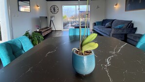 Ein modernes Wohnzimmer mit einem dunkel marmornen Tisch, einer blauen Orchideen-Vase und Blick ins Freie durch ein großes Fenster.