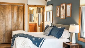 Ein Schlafzimmer mit Bett, Holzschrank und angrenzendem Badezimmer, das durch eine offene Tür sichtbar ist.